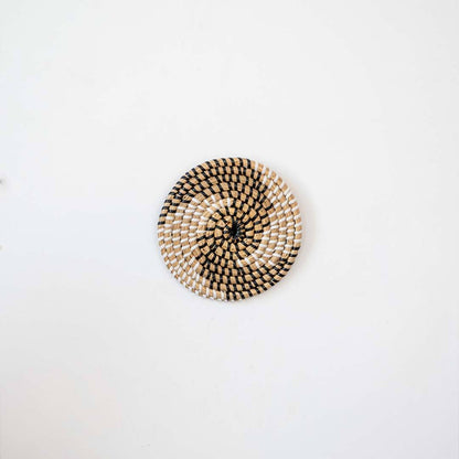 Handwoven seagrass round wall basket decor in natural beige with black spiral woven pattern displayed on white background.