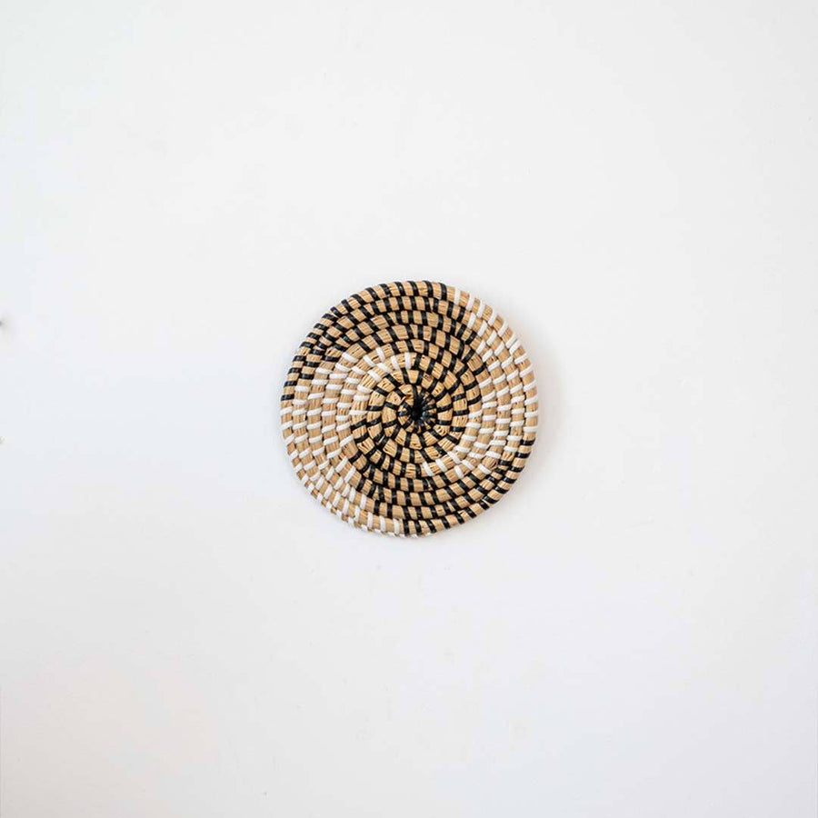 Handwoven seagrass round wall basket decor in natural beige with black spiral woven pattern displayed on white background.
