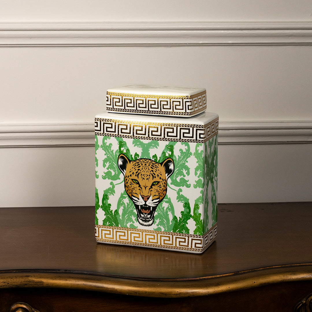 Decorative glass storage jar with tiger artwork and gold lid placed on wooden table against neutral wall background highlighting bold artistic home decor accent.