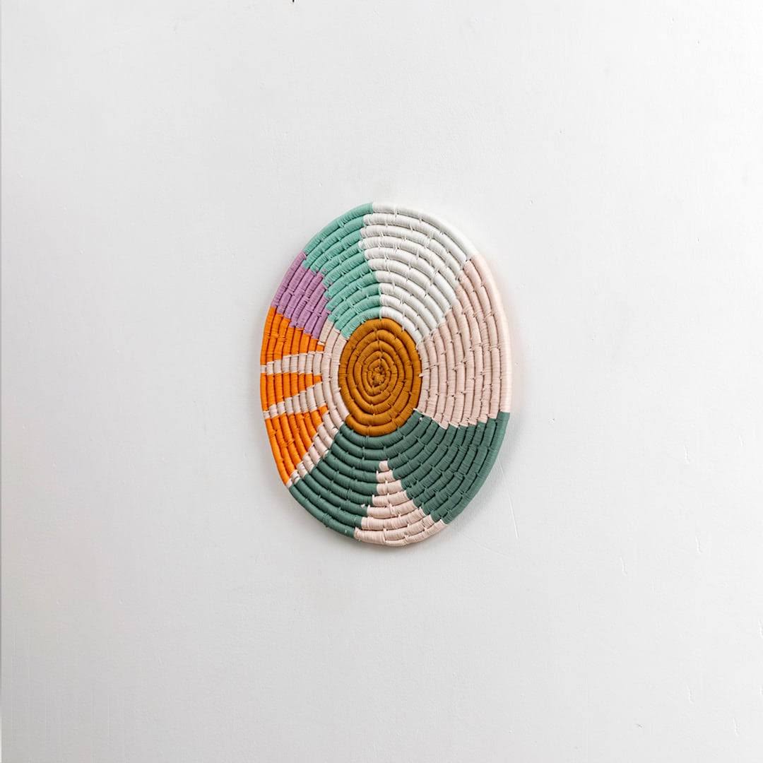 Round handcrafted multicolor seagrass wall basket with orange green cream and white pattern on white background image.