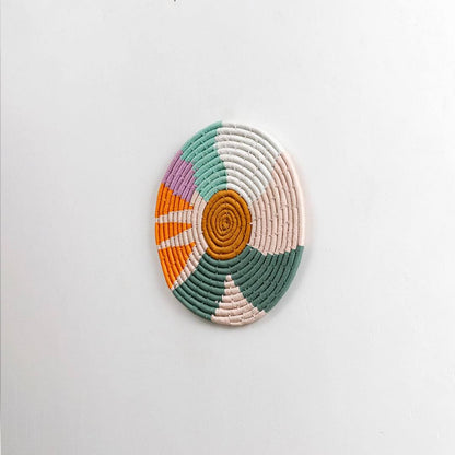 Round handcrafted multicolor seagrass wall basket with orange green cream and white pattern on white background image.