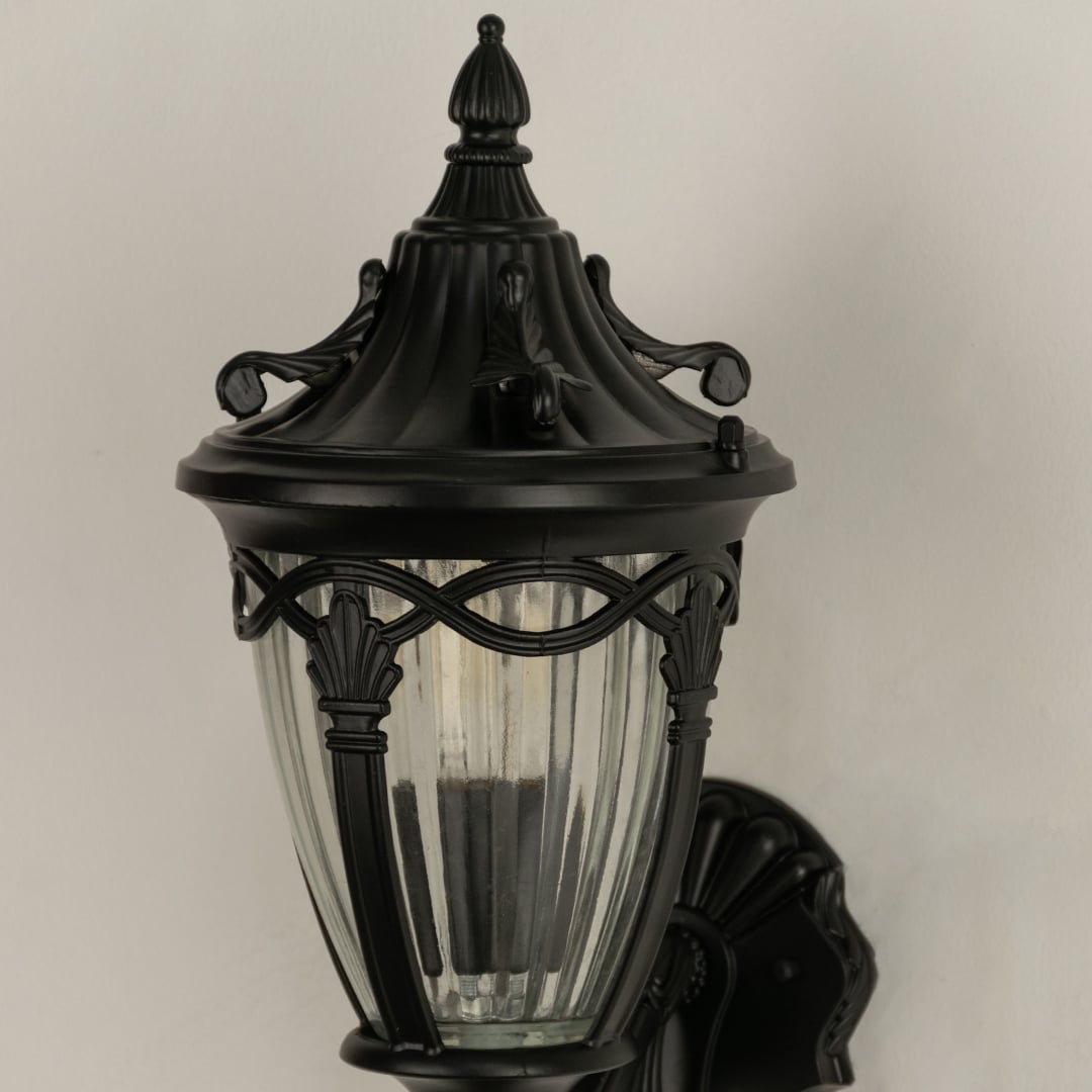 Closeup of black outdoor wall lantern highlighting the ribbed clear glass panels and ornate metal top ideal for enhancing classic porch and entryway decor.