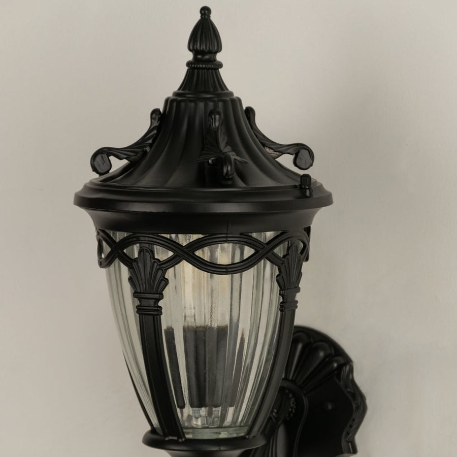 Closeup of black outdoor wall lantern highlighting the ribbed clear glass panels and ornate metal top ideal for enhancing classic porch and entryway decor.