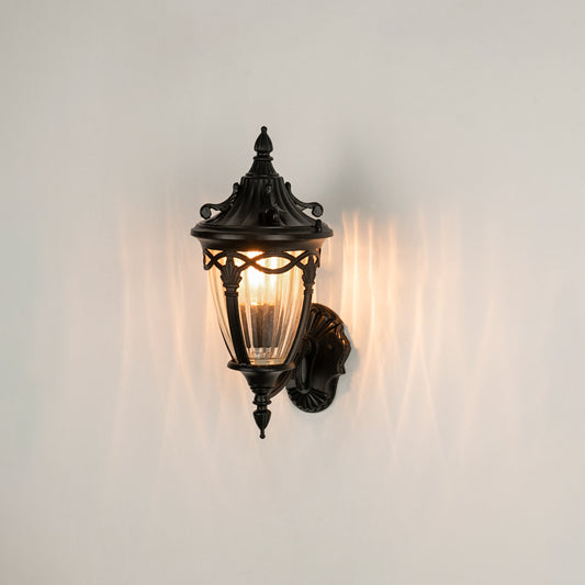 Black metal outdoor wall light on white background with ribbed glass shade casting an elegant pattern for entry decor.
