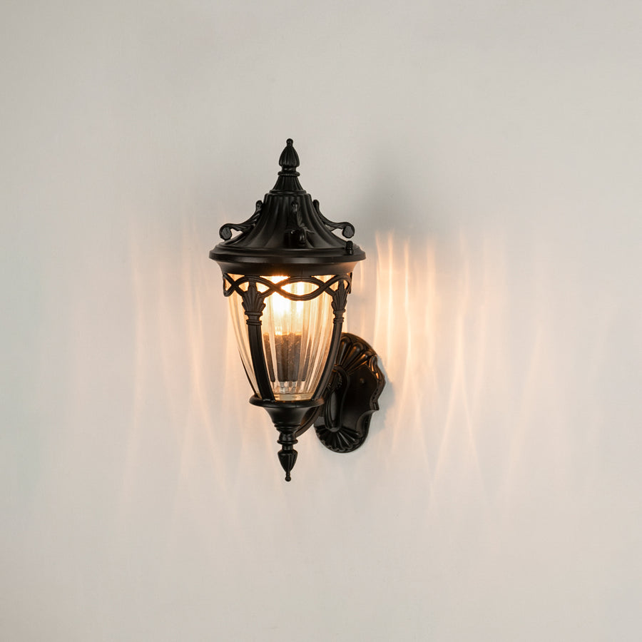Black metal outdoor wall light on white background with ribbed glass shade casting an elegant pattern for entry decor.