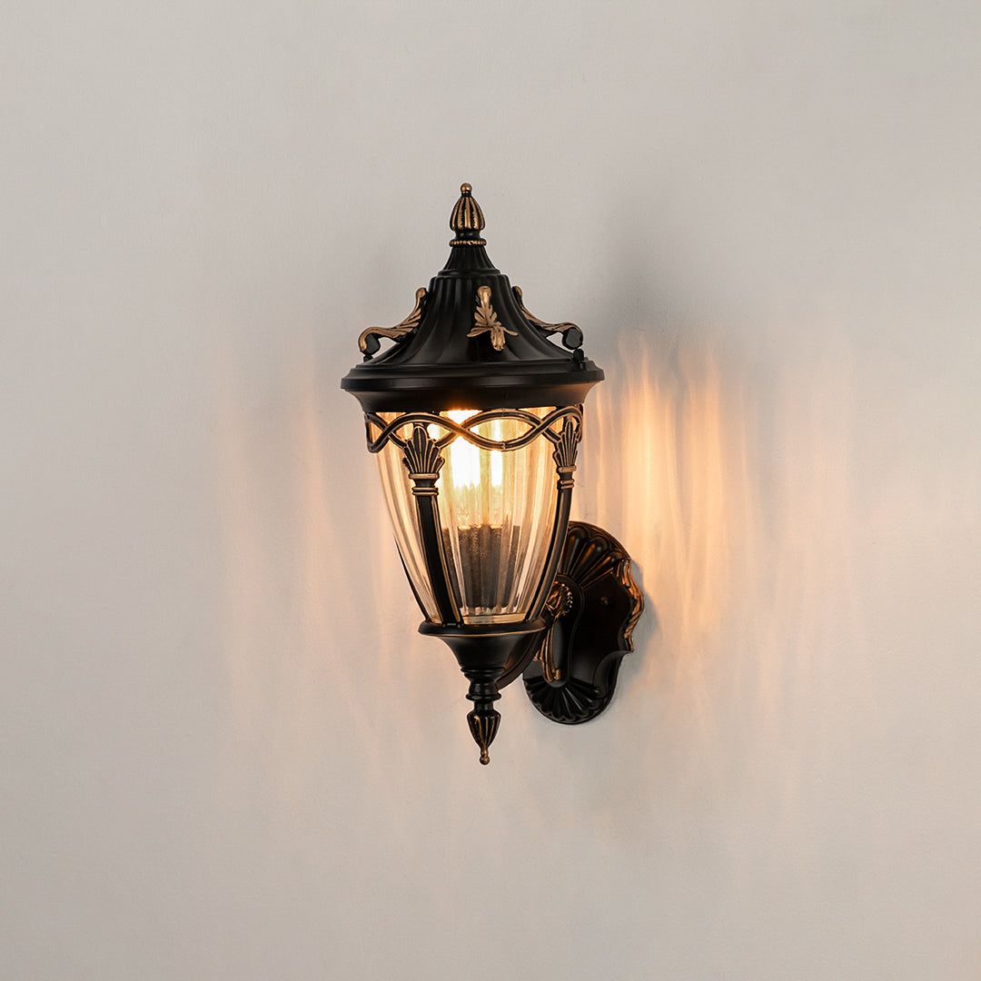 Antique bronze outdoor wall light on white background with ribbed glass shade casting a warm radial glow for patio decor.