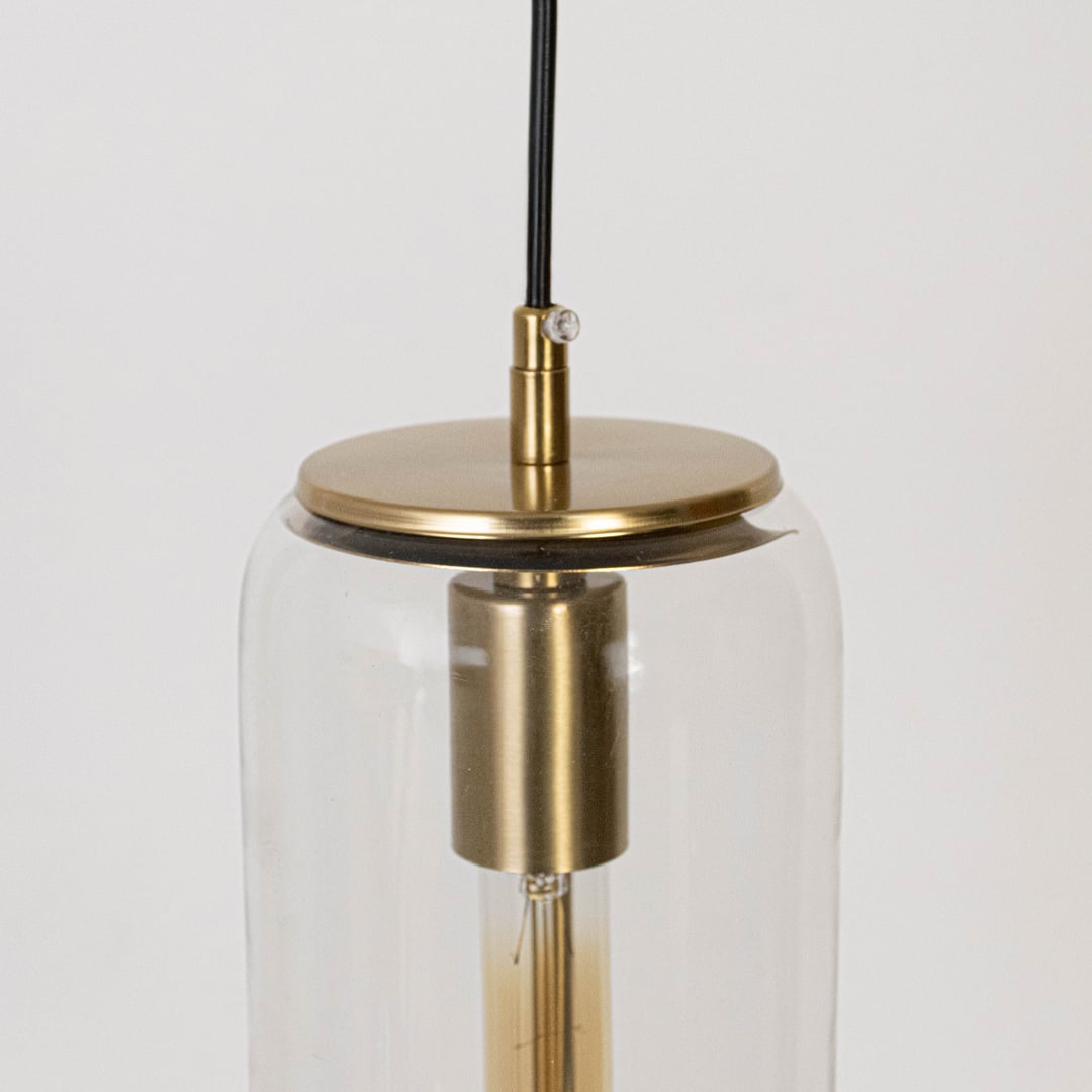 Closeup of pendant light with transparent cylindrical glass shade and gold finish holder for modern home lighting.