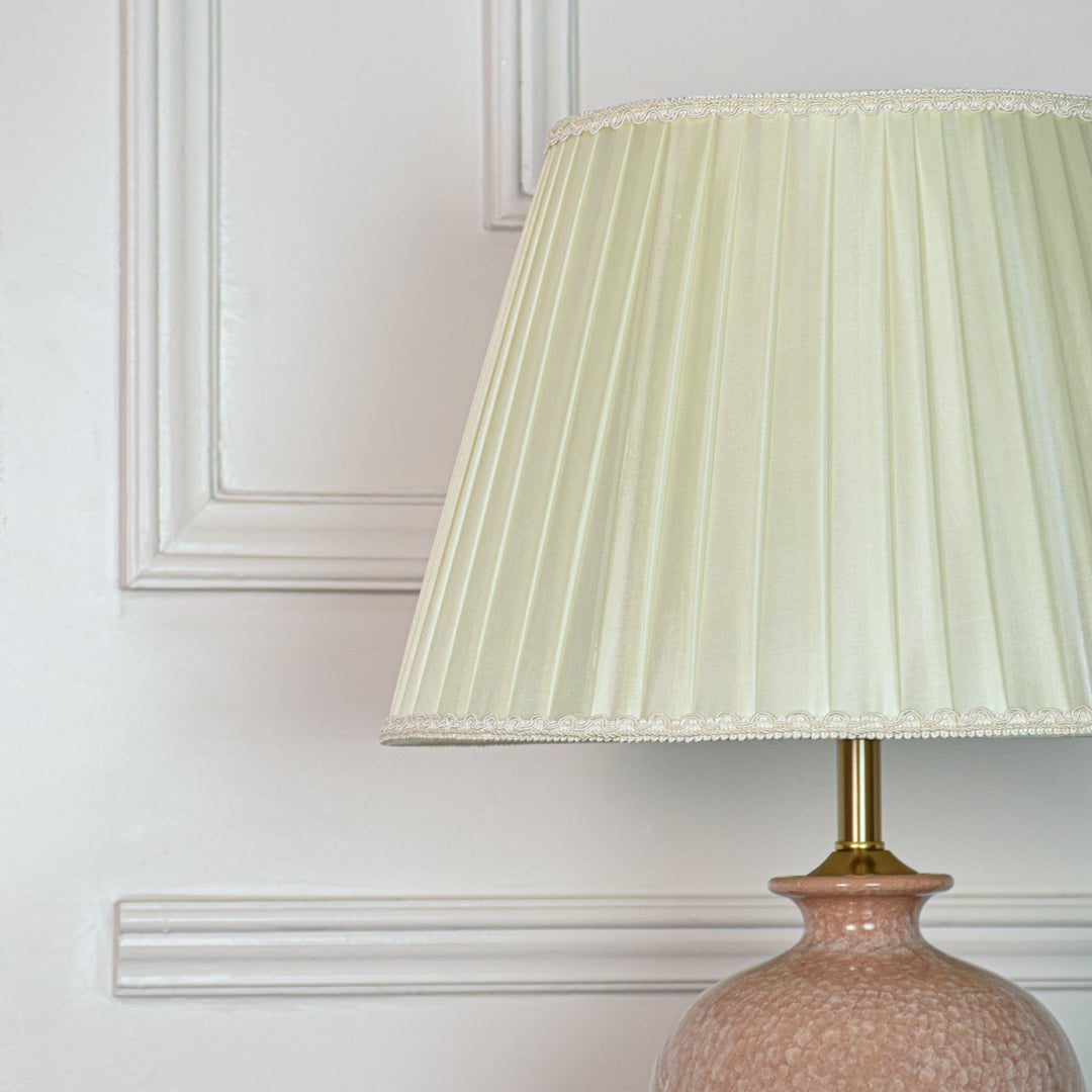 Closeup of pink ceramic table lamp showing textured glazed surface elegant curved shape and gold metal base detailing.