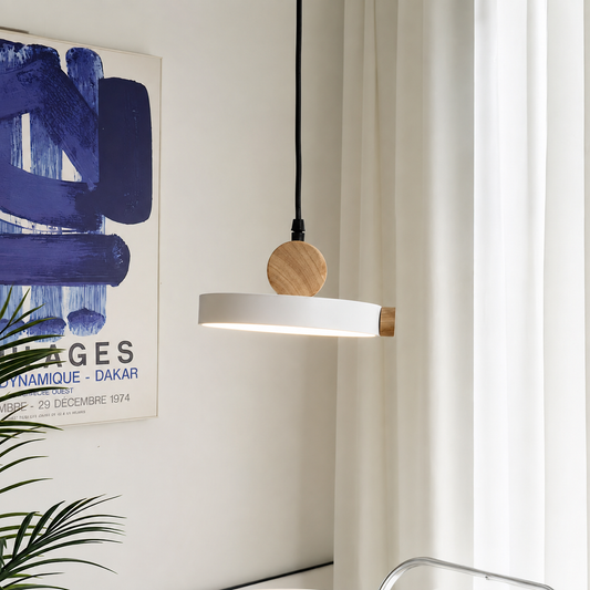 A modern linear pendant light with a white rectangular shade and natural wood accents, hanging from a black cord in a bright room next to a window with white curtains.
