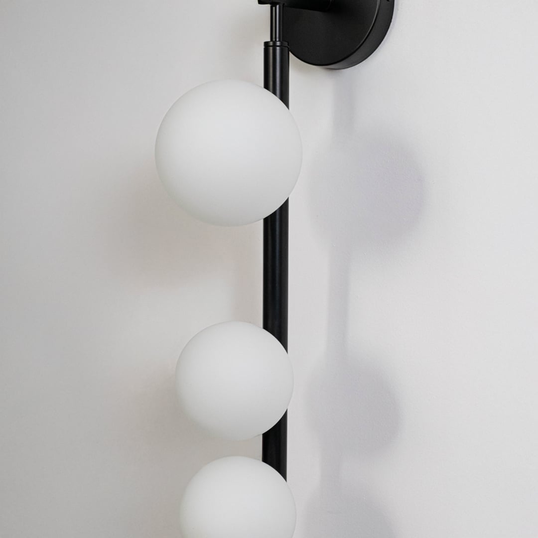 Closeup of black wall sconce with three frosted glass globes sleek vertical rod frame highlighting modern craftsmanship and style.
