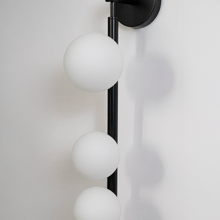 Closeup of black wall sconce with three frosted glass globes sleek vertical rod frame highlighting modern craftsmanship and style.