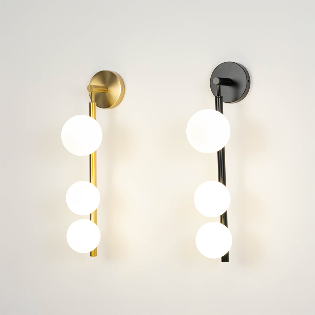Set of black and gold wall sconces with three frosted glass globes glowing brightly displayed together on plain white background view.