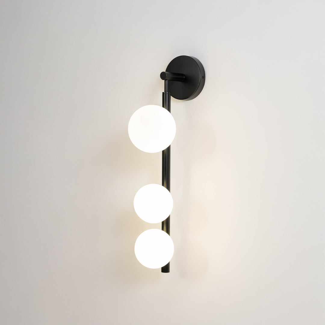 Modern wall light in black metal finish with three globe bulbs for bedroom or living room decor lighting white background.