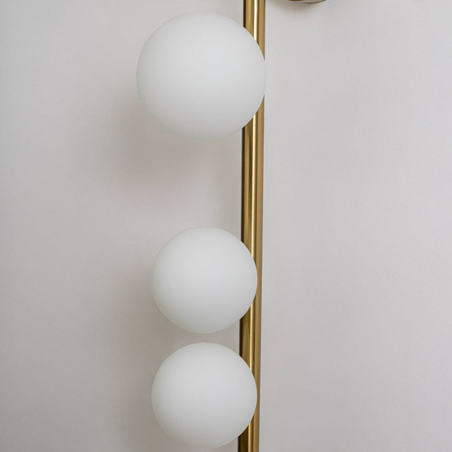 Closeup of luxury gold wall sconce with three frosted glass globes and sleek metal rod frame showing modern craftsmanship detail.