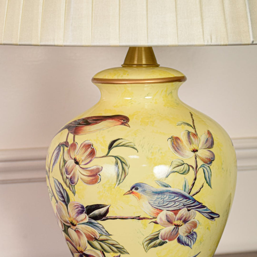 Closeup of yellow ceramic table lamp highlighting detailed floral bird artwork smooth glazed finish and gold metal base.