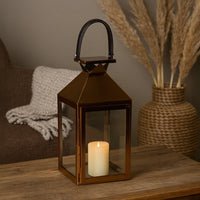 Copper metal lantern with glowing candle styled on wooden table for warm rustic home decor ambiance.