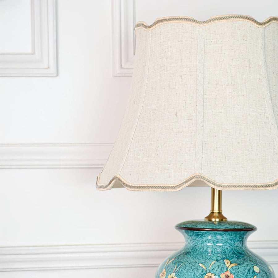 Closeup of teal ceramic table lamp highlighting intricate floral detailing textured glaze finish and gold metal base accents.