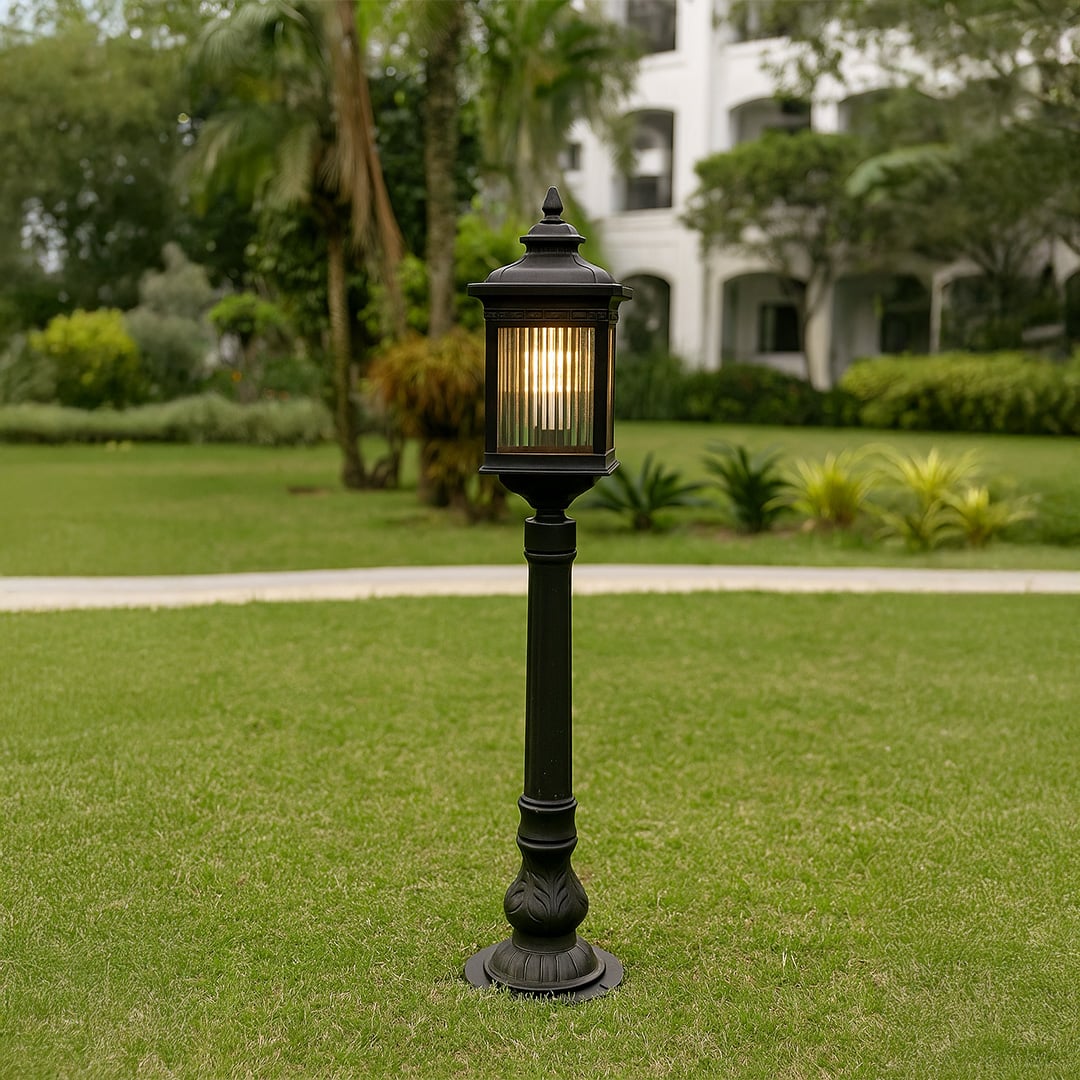 Outdoor garden post light in black metal with glass panels placed on lawn pathway providing warm illumination and classic landscape lighting style.