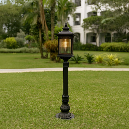 Outdoor garden post light in black metal with glass panels placed on lawn pathway providing warm illumination and classic landscape lighting style.