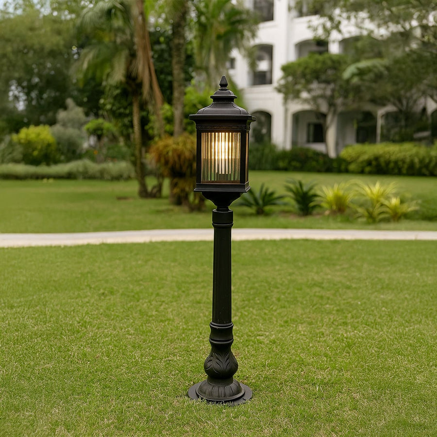 Outdoor garden post light in black metal with glass panels placed on lawn pathway providing warm illumination and classic landscape lighting style.