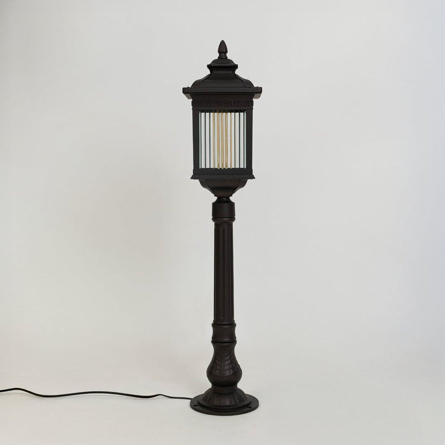 A modern black outdoor bollard light shown on a white background with the light off highlighting its clean rectangular structure clear ribbed glass panels and sturdy base.