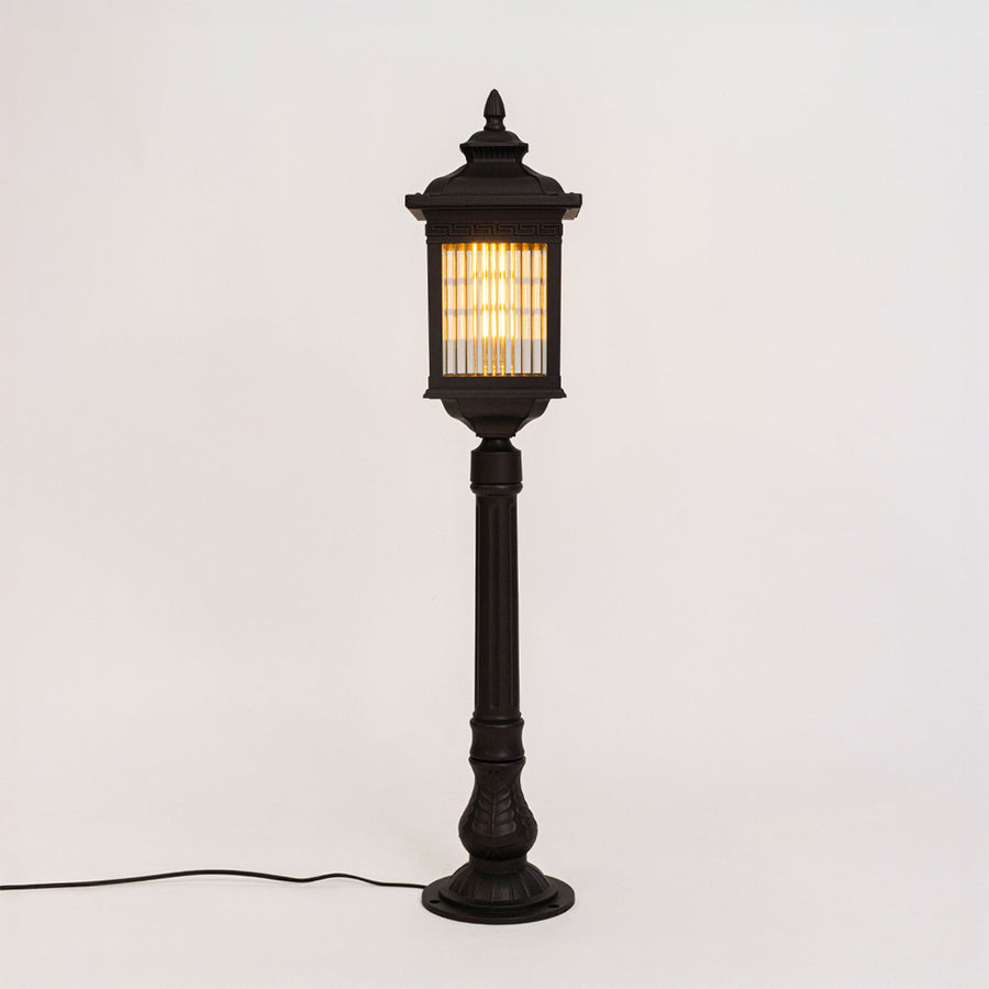 Vintage black outdoor bollard light with warm glowing panels for luxury exterior decor styling use.