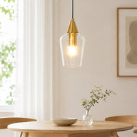 Modern gold brass metal and clear glass bell pendant hanging light fixture over wooden dining room table for kitchen styling.