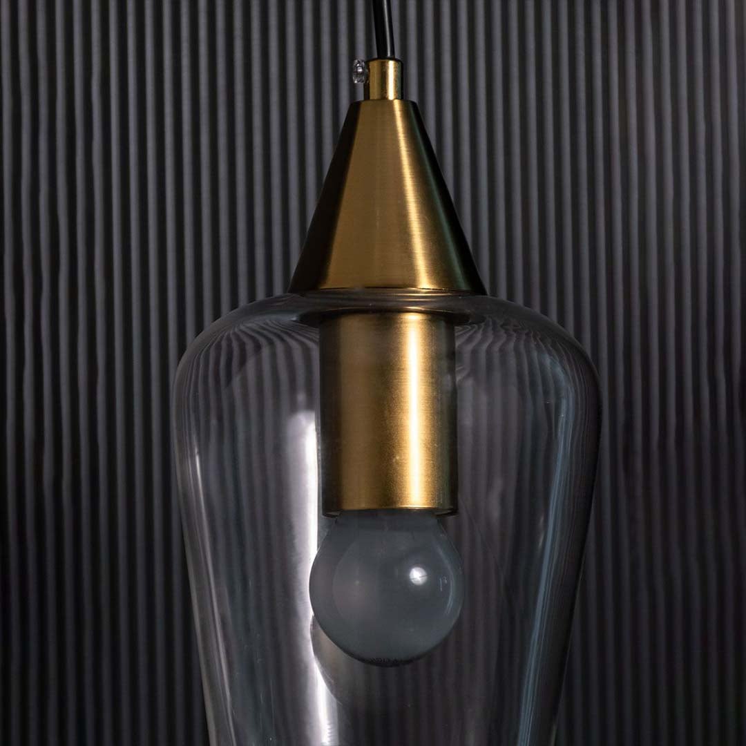 A clear glass pendant light with a gold top shown against a textured black background.