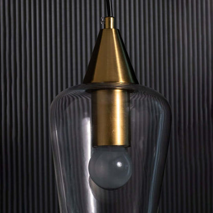 A clear glass pendant light with a gold top shown against a textured black background.