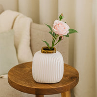 White ribbed ceramic vase with pink flower placed on wooden table adding soft elegant touch to cozy home Decor setting.