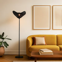 Black floor lamp with woven rattan shade beside mustard sofa in modern living room warm ambient lighting.