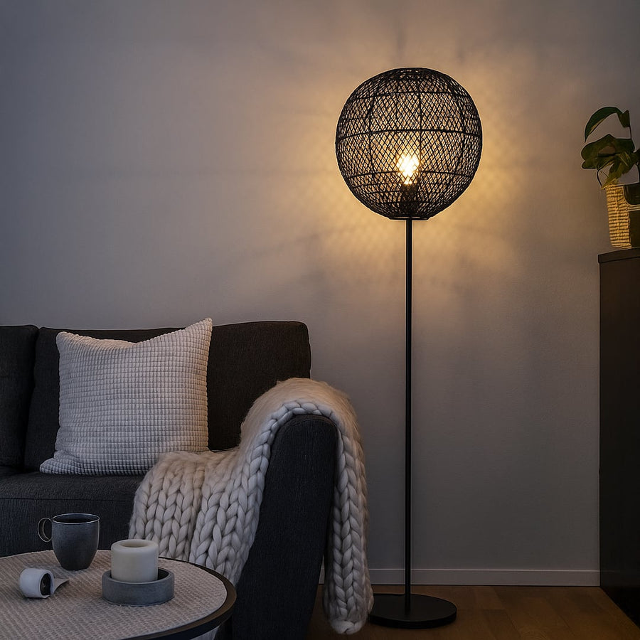 Black floor lamp with woven rattan globe shade beside dark sofa in modern living room warm ambient lighting.