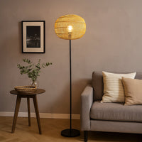 Black floor lamp with woven rattan shade beside grey sofa and wooden table in cozy modern living room.