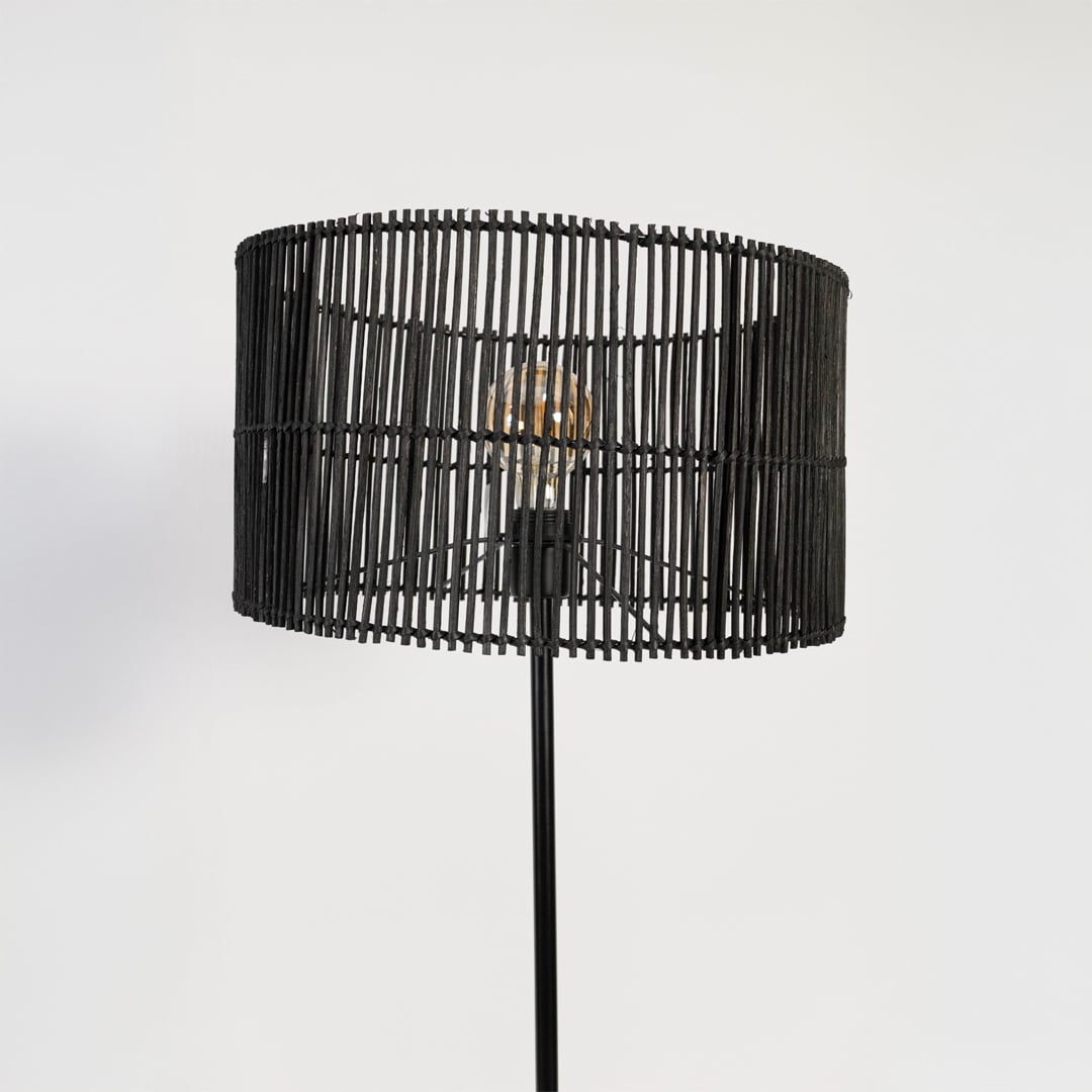 Closeup of black floor lamp with cylindrical woven rattan shade highlighting natural texture and sleek design.