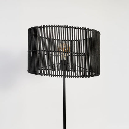 Closeup of black floor lamp with cylindrical woven rattan shade highlighting natural texture and sleek design.