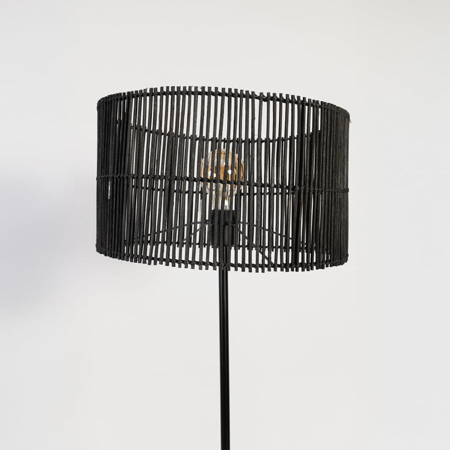 Closeup of black floor lamp with cylindrical woven rattan shade highlighting natural texture and sleek design.