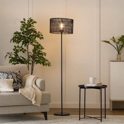 Black floor lamp with cylindrical rattan shade beside beige sofa in modern living room warm ambient lighting.