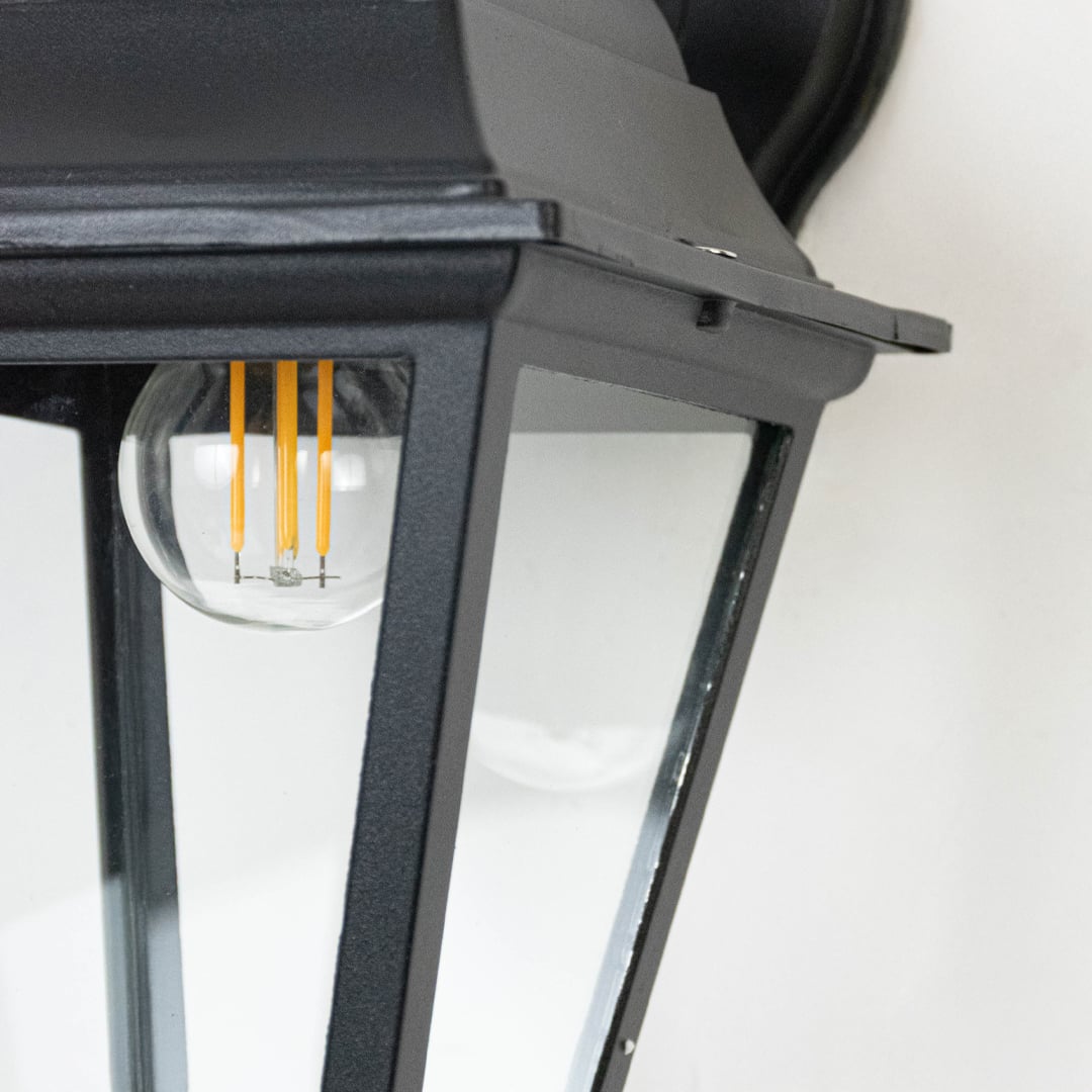 Closeup of outdoor wall lantern showing black metal body and clear glass panels highlighting fine details and texture.