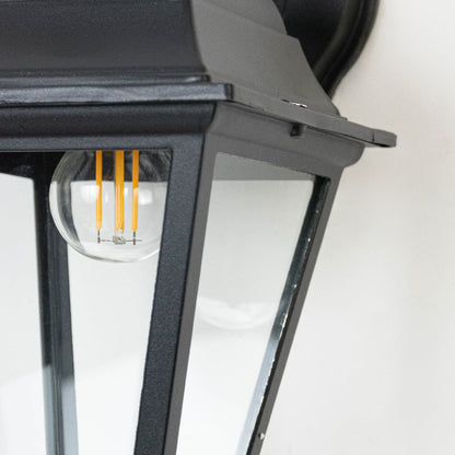 Closeup of outdoor wall lantern showing black metal body and clear glass panels highlighting fine details and texture.