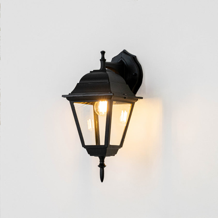 Black metal outdoor wall light on white background with warm glow for elegant exterior entryway decor.