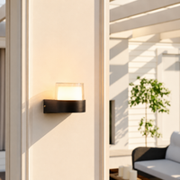 Modern black aluminum half cylinder glass wall sconce fixture on cream stucco pillar for contemporary patio exterior decor.