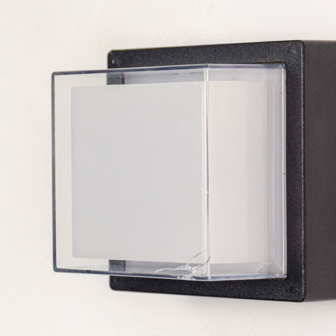 Closeup of black square exterior wall light showcasing sturdy metal base clear glass cover and compact build.
