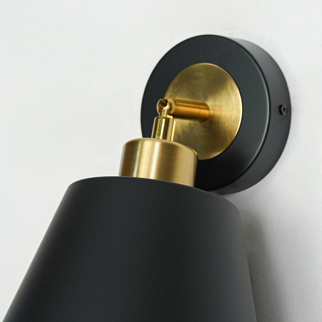 Closeup of black and gold metal wall light base with cone shade for luxury modern interior decor styling.