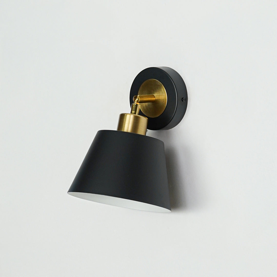 Modern black and gold metal wall light mounted on white wall for stylish bedroom and hallway decor styling.