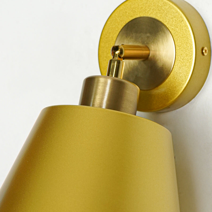 Closeup of gold metal wall light with cone shade showcasing smooth finish and premium detailing for modern interior decor styling.