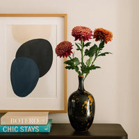 Glass flower vase in dark finish placed on console table with books and wall art adding artistic touch to modern living space.