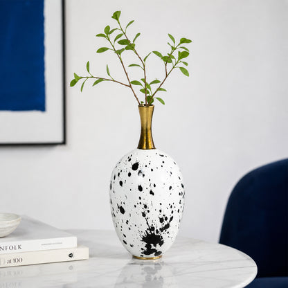 White and black ceramic flower vase with gold neck placed on marble table for elegant home decor.