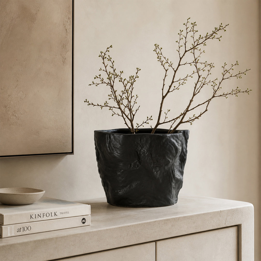 Black textured ceramic planter bowl with branches placed on table for modern minimalist home decor styling.