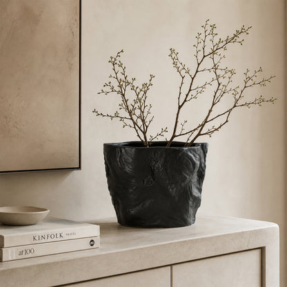 Black textured ceramic planter bowl with branches placed on table for modern minimalist home decor styling.
