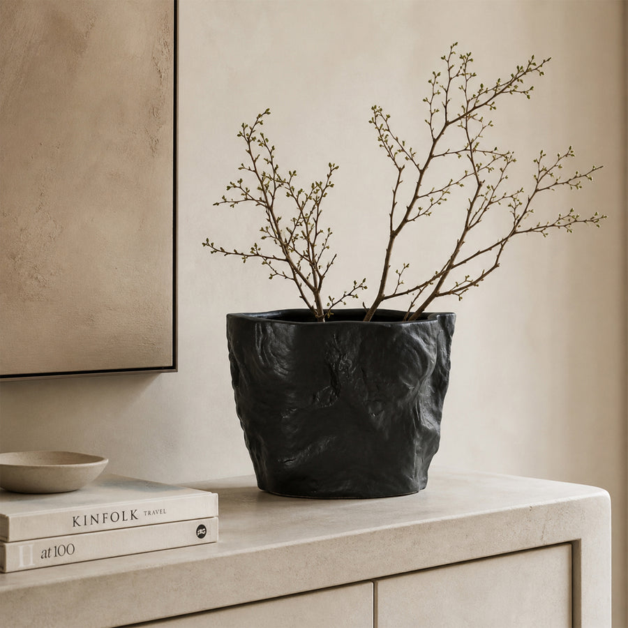 Black textured ceramic planter bowl with branches placed on table for modern minimalist home decor styling.